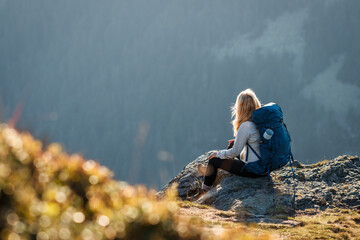 Woman with backpack sitting on the mountain peak. Resting during hike