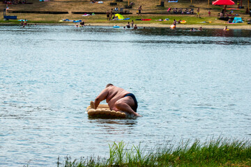 An obese man tries to climb out on an air mattress on a lake