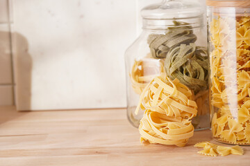 Variety of dry italian pasta in glass jars on kitchen cabinet with wooden top: fusilli,...