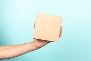 Woman hand show small brown rectangular cardboard box on light blue background. Mockup parcel box....