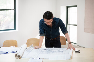 Businessman analyzing blueprint at desk in creative office