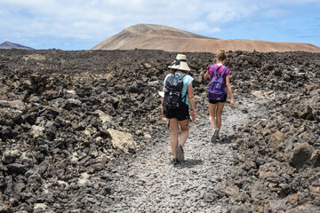 Two girls walking towards the Caldera Blanca volcano between lava and volcanic rocks in Lanzarote