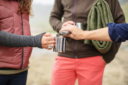 Cropped image of man pouring alcohol in woman's mug on beach