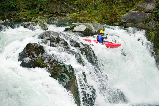 Kayaker paddling through waterfall in forest