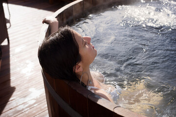 Woman relaxing in wooden bathtub on sunny day