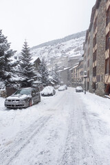 snow covered streets in a mountain village with parked cars partially covered by snow, cars with snow chains, Soldeu, Andorra,  portrait