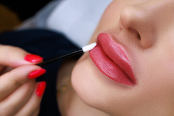 close-up of the model's lips with permanent make-up, the master wipes the model's lips with a...