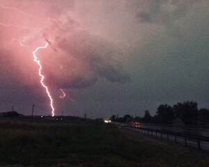Lightning strikes the ground. Cars move along the track. Evening thunderstorm. High-quality photo