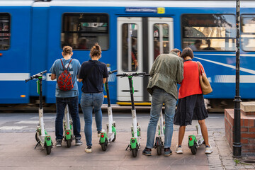 Four people are going to use an electric scooter in the city, a city tram passes by, activation of...
