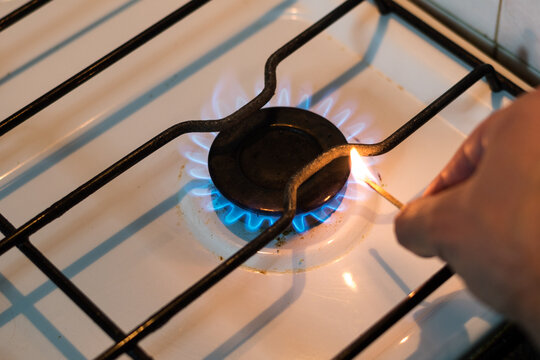 hombre encendiendo con un fosforo una hornalla de una cocina blanca usada