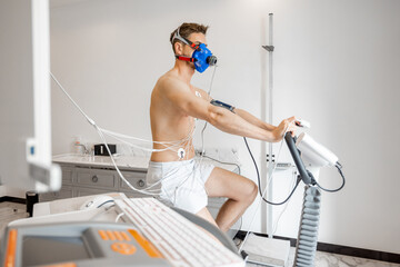 Man athlete with breath mask and electrodes training on bike simulator, examining his...