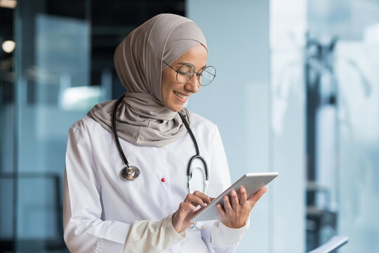 Female doctor in hijab works in modern clinic office, Muslim female doctor uses tablet computer, nurse in medical white coat and glasses with stethoscope.