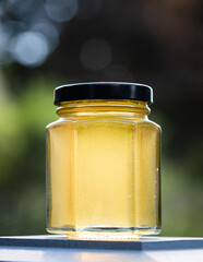 Small jar of honey outside against a green background