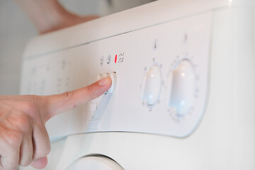 Hand presses the button on the panel of washing machine closeup