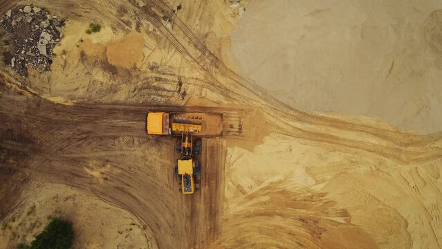 Aerial top down view of an excavator loading sand into a dump truck in a sand quarry