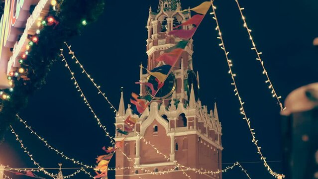 Festive garlands against the background of the night sky and the Kremlin Spasskaya Tower with a clock on Red Square create a New Year's mood. Shot in motion