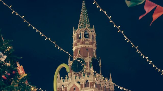 Festive garlands and a Christmas tree with toys against the Kremlin Spasskaya Tower with a clock on Red Square create a festive, New Year's mood. Shot in motion
