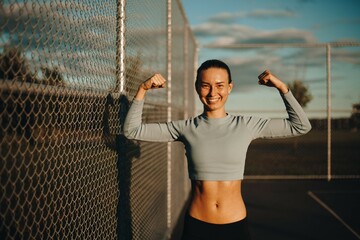 Happy woman on the basketball field. A young woman shows her muscles in her arms. Portrait photo of an athletic woman. Fitness sporty woman showing her well trained body 

