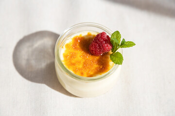 Fresh creme brulee dessert decorated with fresh berries and mint on a linen tablecloth in bright sunshine.