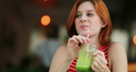 Young woman drinking detox green juice, redhair pretty girl holding healthy natural drink