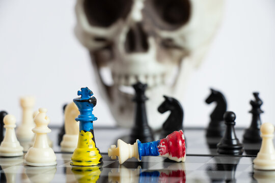 Chess with a painted flag of Russia and Ukraine on a chessboard and a head of a skeleton in the background, a death game between the two countries of Ukraine and Russia, war 2022