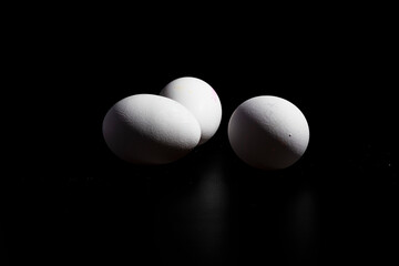 tres huevos blancos de gallina, sobre fondo negro 