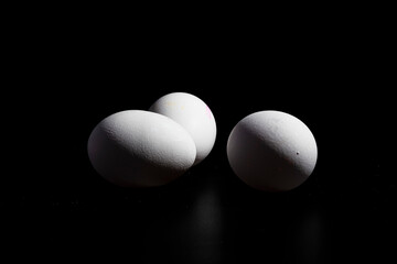 tres huevos blancos de gallina, sobre fondo negro 
