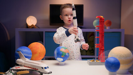 Little blonde boy kid plays with spaceship from constructor, flies near planets of solar system in...