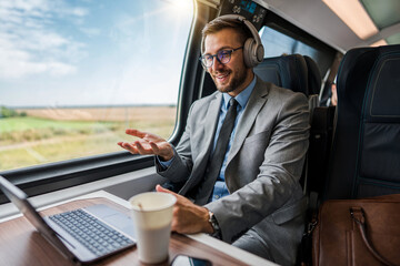 Handsome businessman is having a good time while traveling by high-speed train. He is using laptop...