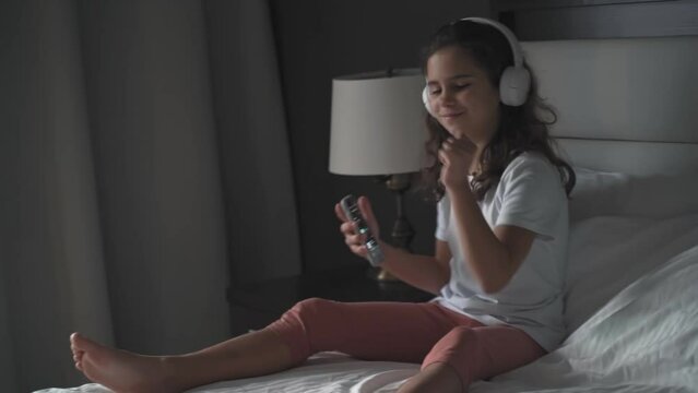 beautiful teenage girl listens to music with headphones and dancing in bed in the morning. Happy adult kid wakes up and listens to dance music