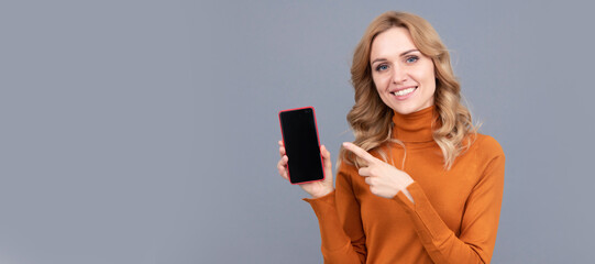Naklejka premium Happy girl pointing finger at mobile phone. Pointing index finger for advertising. Woman portrait, isolated header banner with copy space.