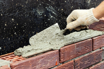 A worker builds a brick wall. Applying cement to brick. Hands in gloves and spatula. selective focus