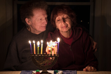 Senior couple celebrating Jewish holiday Hanukkah at home; woman lighting the candles and man looking at her affectionately