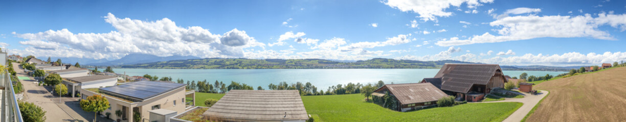 Scenic Swiss countryside with lake, panorama. Beautiful touristic summer scenery in Central Switzerland. Lake Sempach with modern single homes, farms and far off rural villages. Selective focus.
