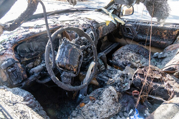 Burned out auto car interior from a fire or explosion or fire bomb or arson showing the melted steering wheel and the devastation.  
