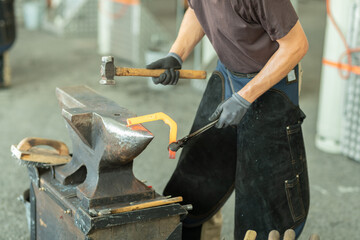 Close-up of blacksmith in apron working with hammer and glowing iron in the workshop