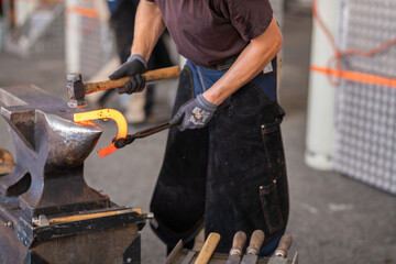 Close-up of blacksmith in apron working with hammer and iron in the workshop