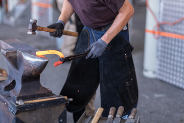 Close-up of blacksmith in apron working with hammer and iron in the workshop