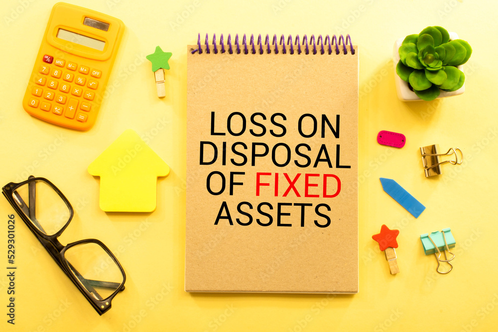 Poster loss on disposal of fixed assets label on notepad with laptop and smartphone on wooden table.