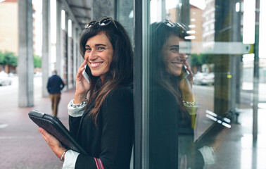 Portrait of happy woman talking on mobile phone while standing by window