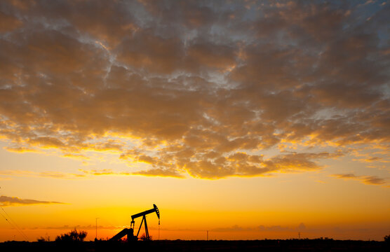 Silhouette oil pump on field against cloudy sky during sunset