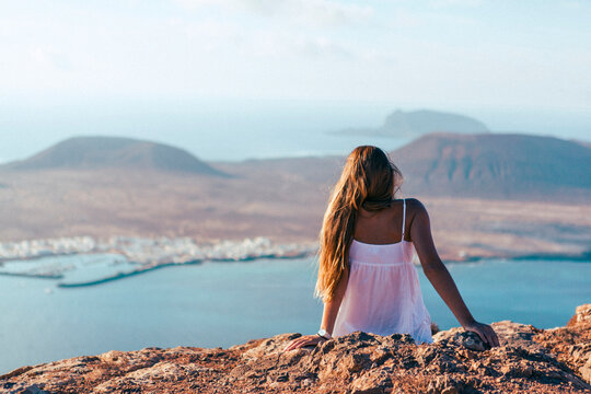 Rear view of woman sitting on mountain against island