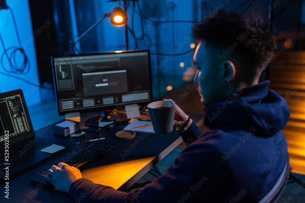 Poster cybercrime, hacking and technology concept - male hacker in dark room drinking coffee and using comp