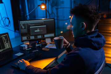 cybercrime, hacking and technology concept - male hacker in dark room drinking coffee and using...