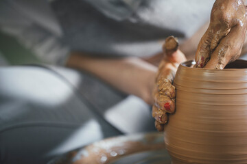 Midsection of female potter shaping clay on spinning wheel at workshop