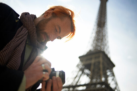 Low angle view of male tourist watching pictures on DSLR camera against Eiffel Tower