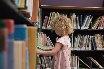 Side view of girl looking at book while standing in library