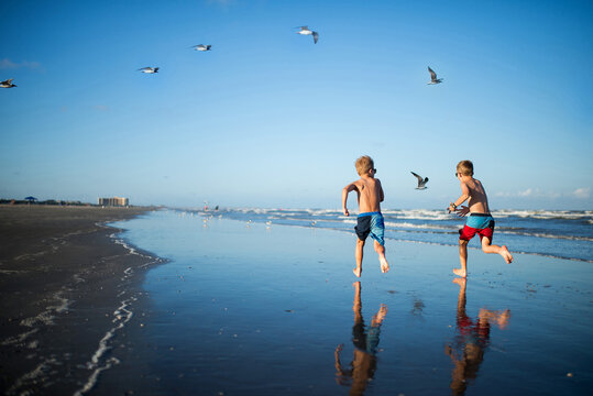 Rear view of brothers running on beach against clear sky