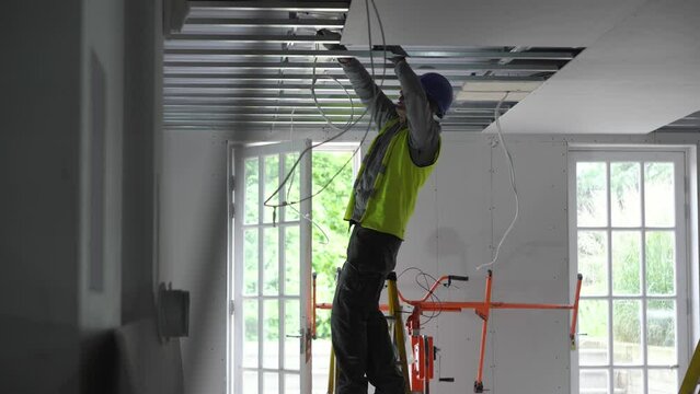 Hard male work on construction site. Two professional workers in special uniforms Contractors Safety Hats repairing ceiling wall inside building. Builders' equipment at workplace. industrial premises