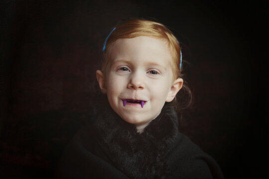 Close-up portrait of girl with vampire teeth standing against black background
